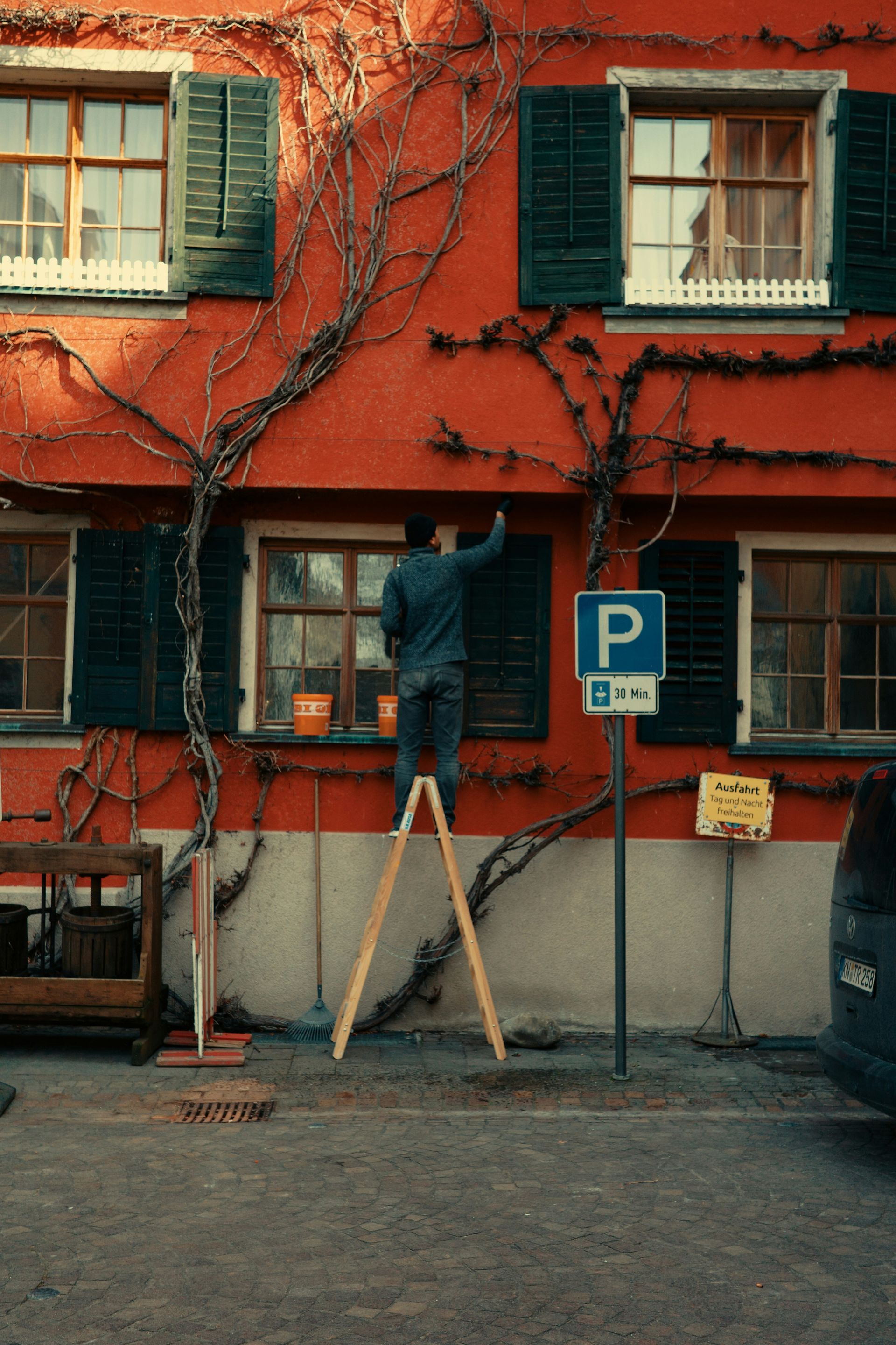 Man painting a red building while standing on a ladder.