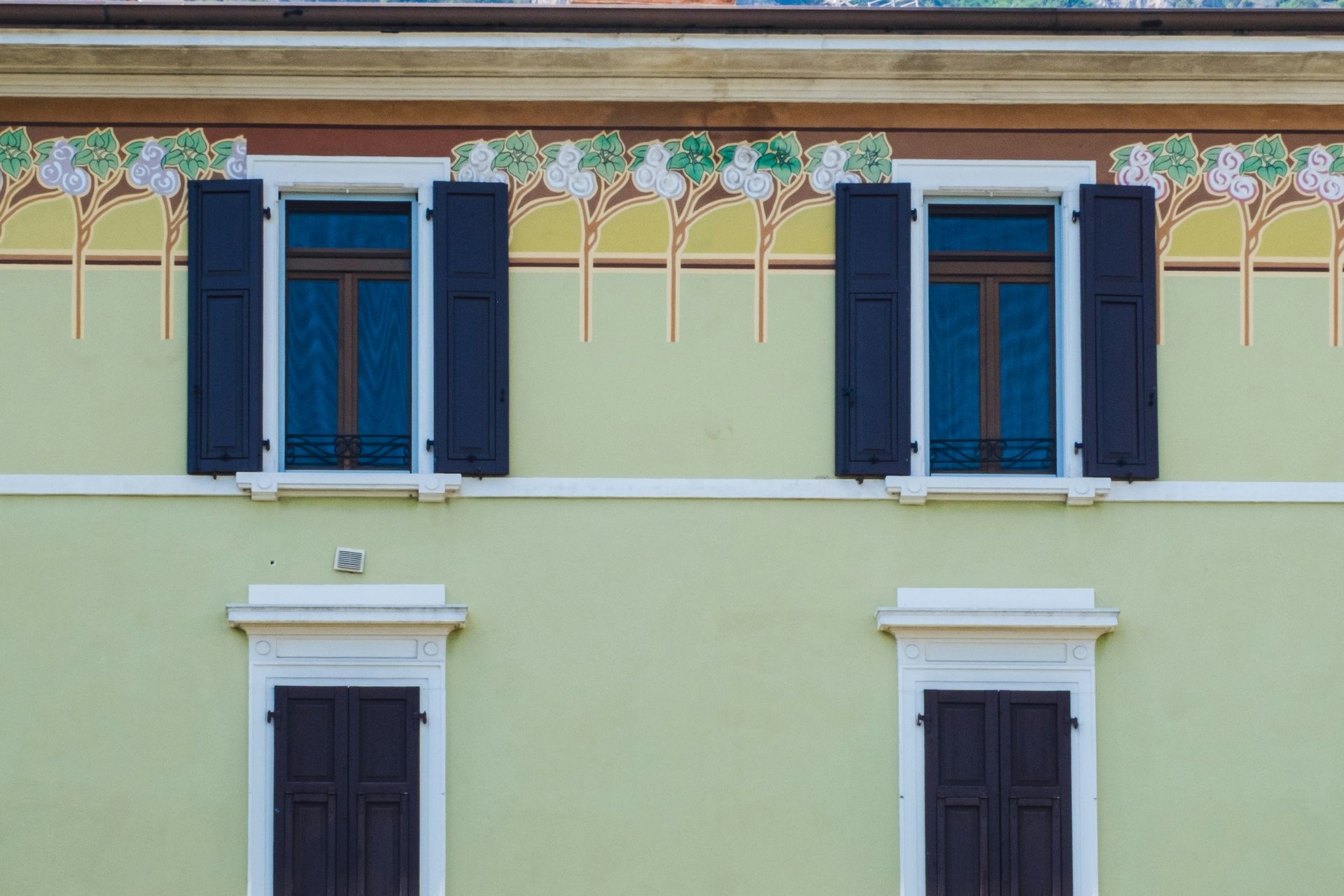 Building facade with four windows, dark shutters, and decorative frieze.