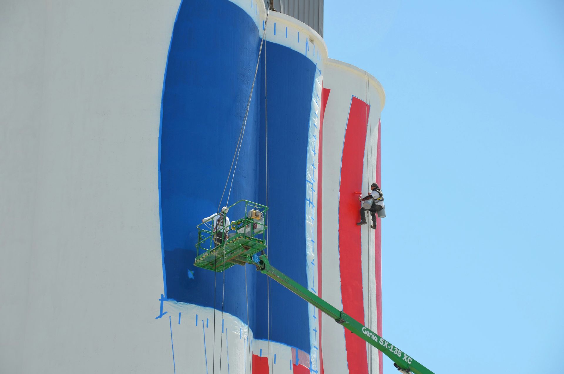 Workers painting a large blue and red striped structure