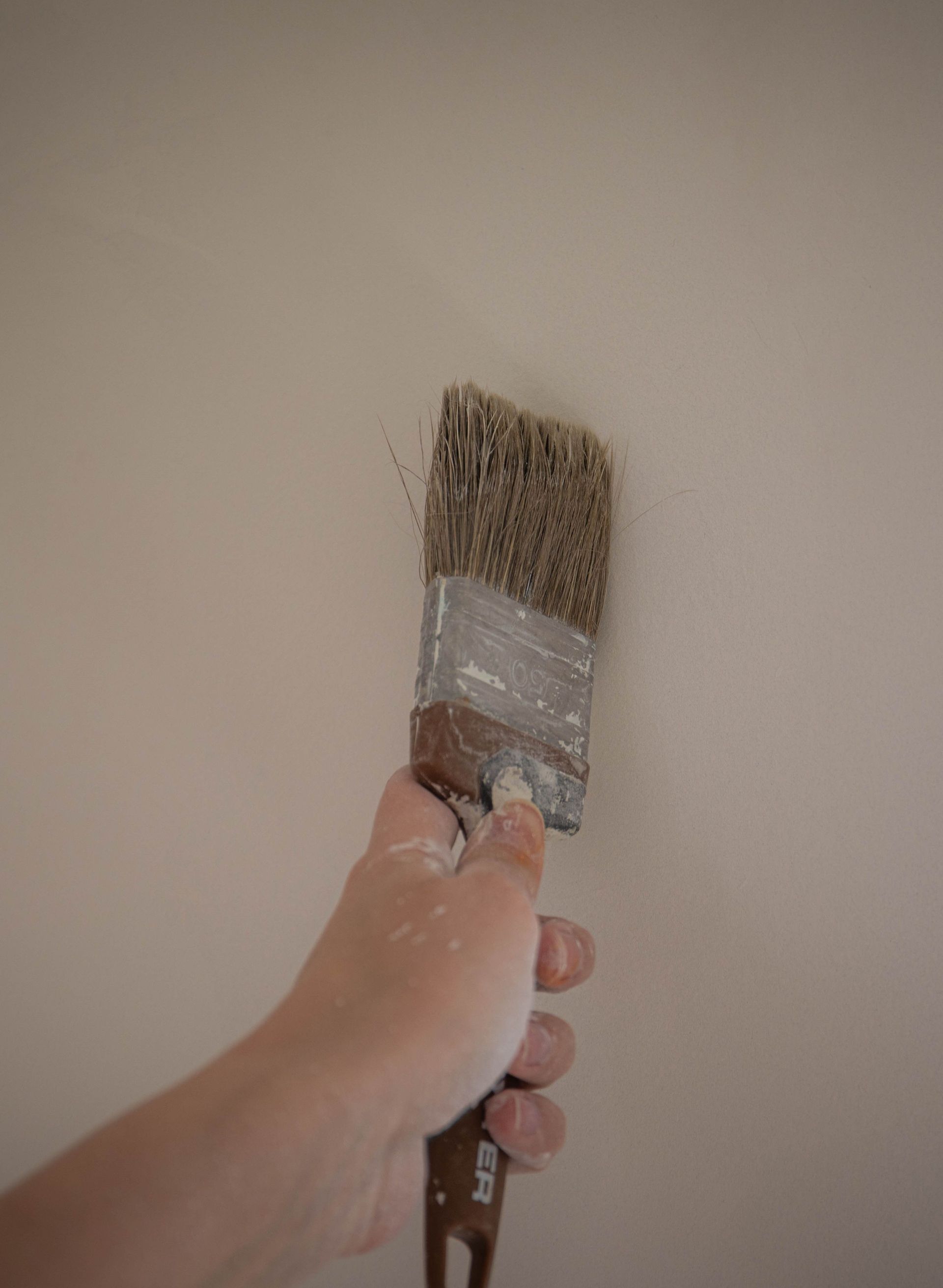A hand painting an interior wall with a large brush, emphasizing DIY home improvement.